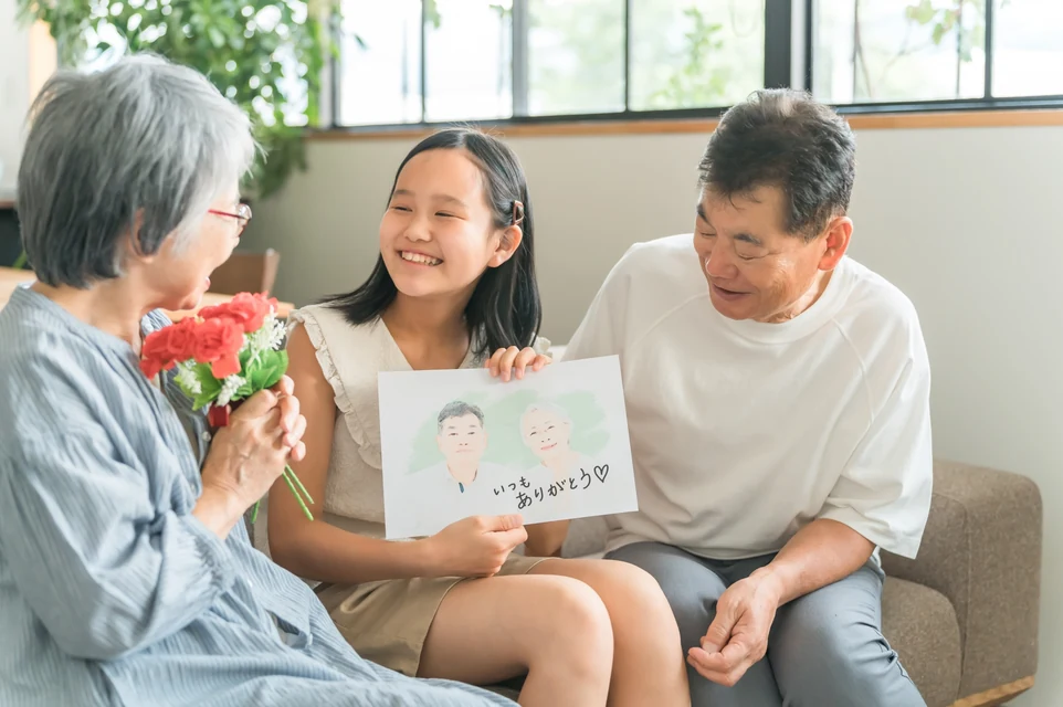 還暦と古希を迎えた家族へ赤と紫を添えた長寿祝いギフトを渡す場面